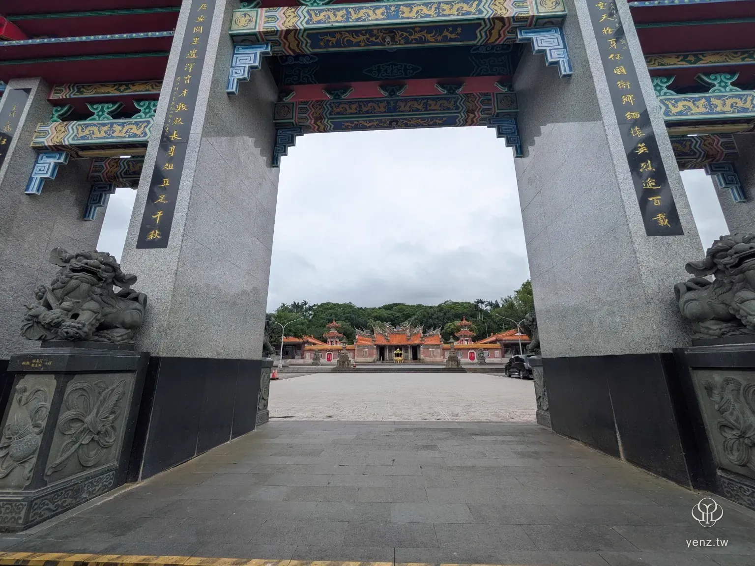 從義民廟牌樓下方往內拍攝，石柱與彩繪樑架形成框景，遠方可見正殿。