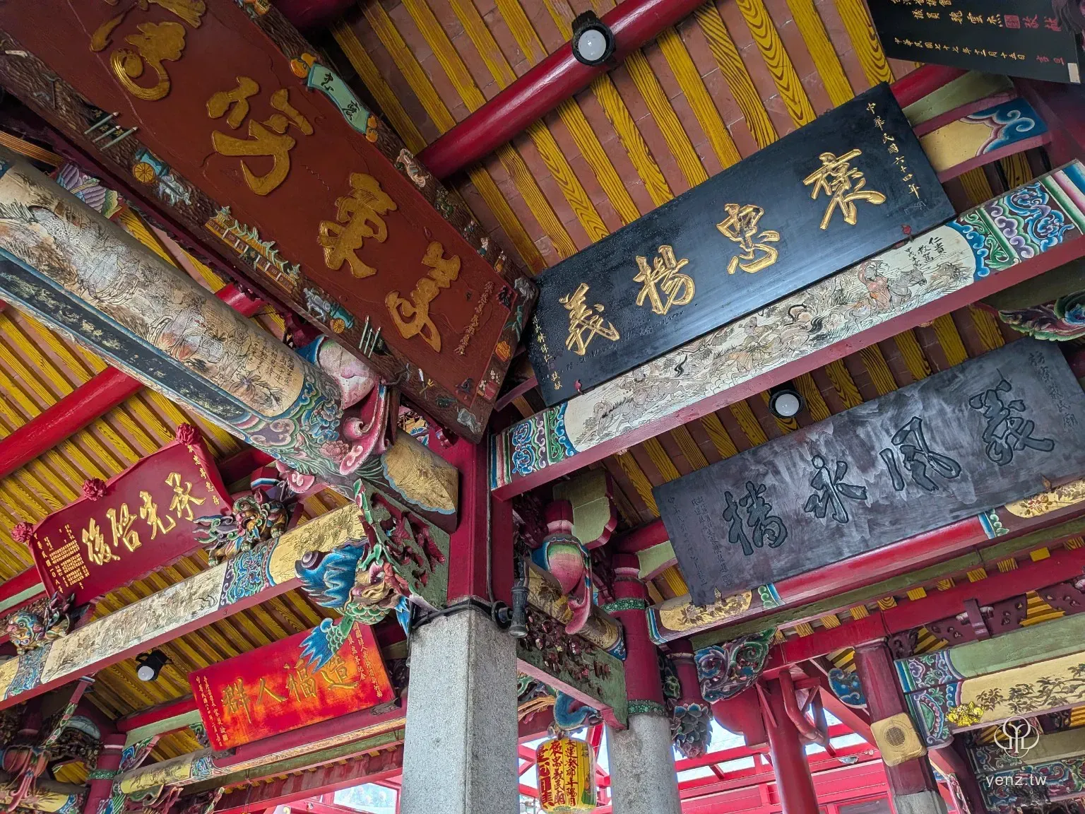 義民廟內部仰拍，多面黑底與紅底金字牌匾懸掛在彩繪木構間。