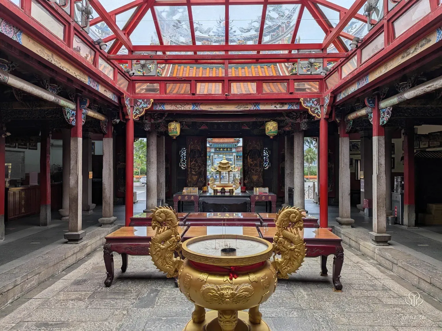 從義民廟內部香爐往外拍攝，前景是金色香爐與供桌，遠方可見牌樓與廟埕。