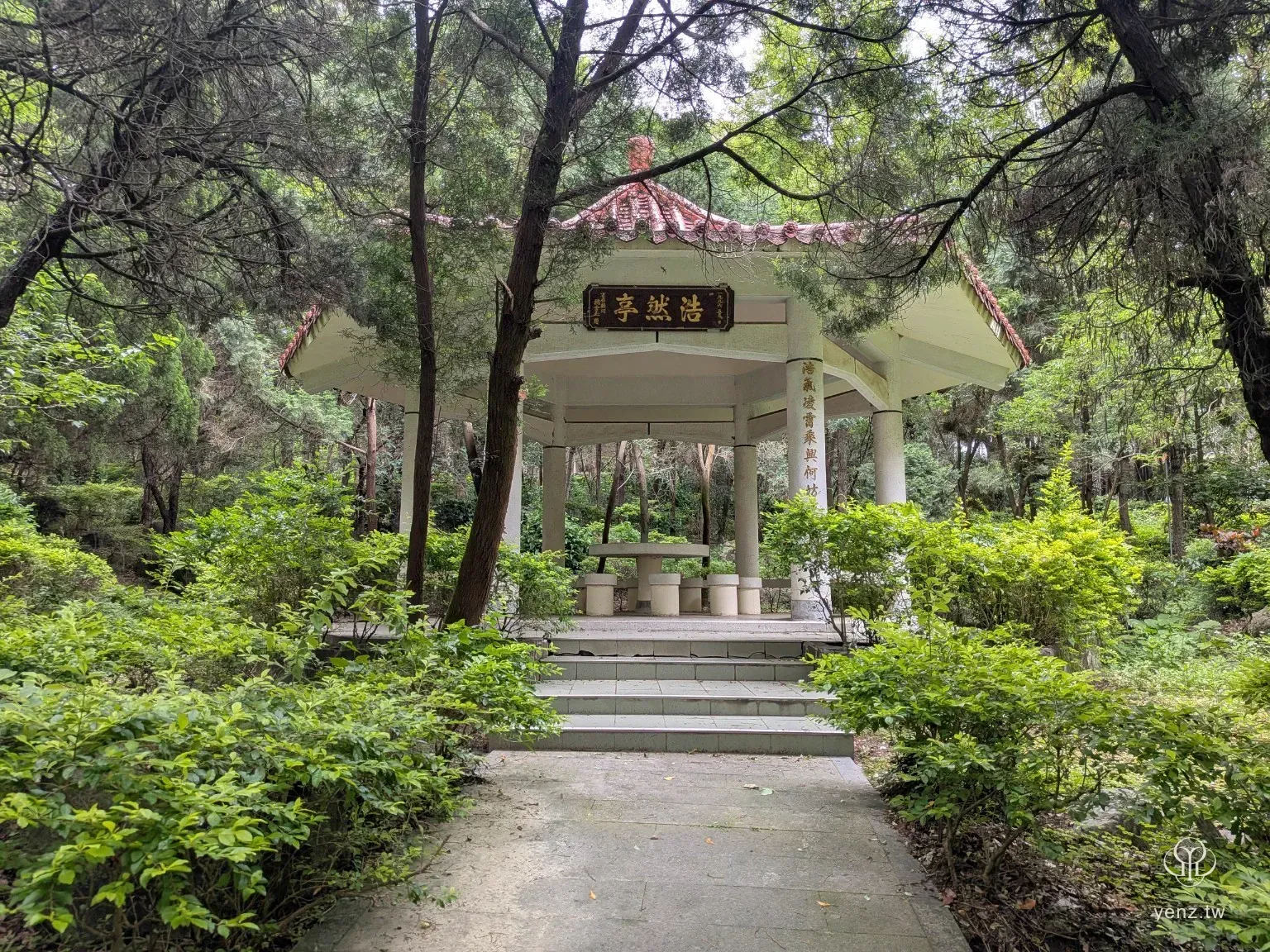 義民廟後花園中的浩然亭，白色亭柱與紅瓦屋頂被樹木與灌木包圍。