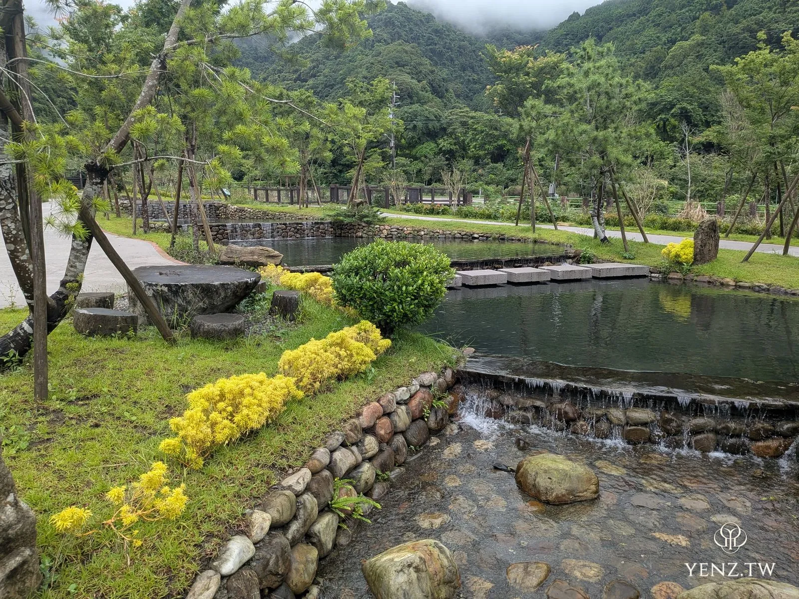 櫸山水水環廊道，階梯狀的生態埤塘、踏石與小落瀑，後方是雲霧繚繞的山。