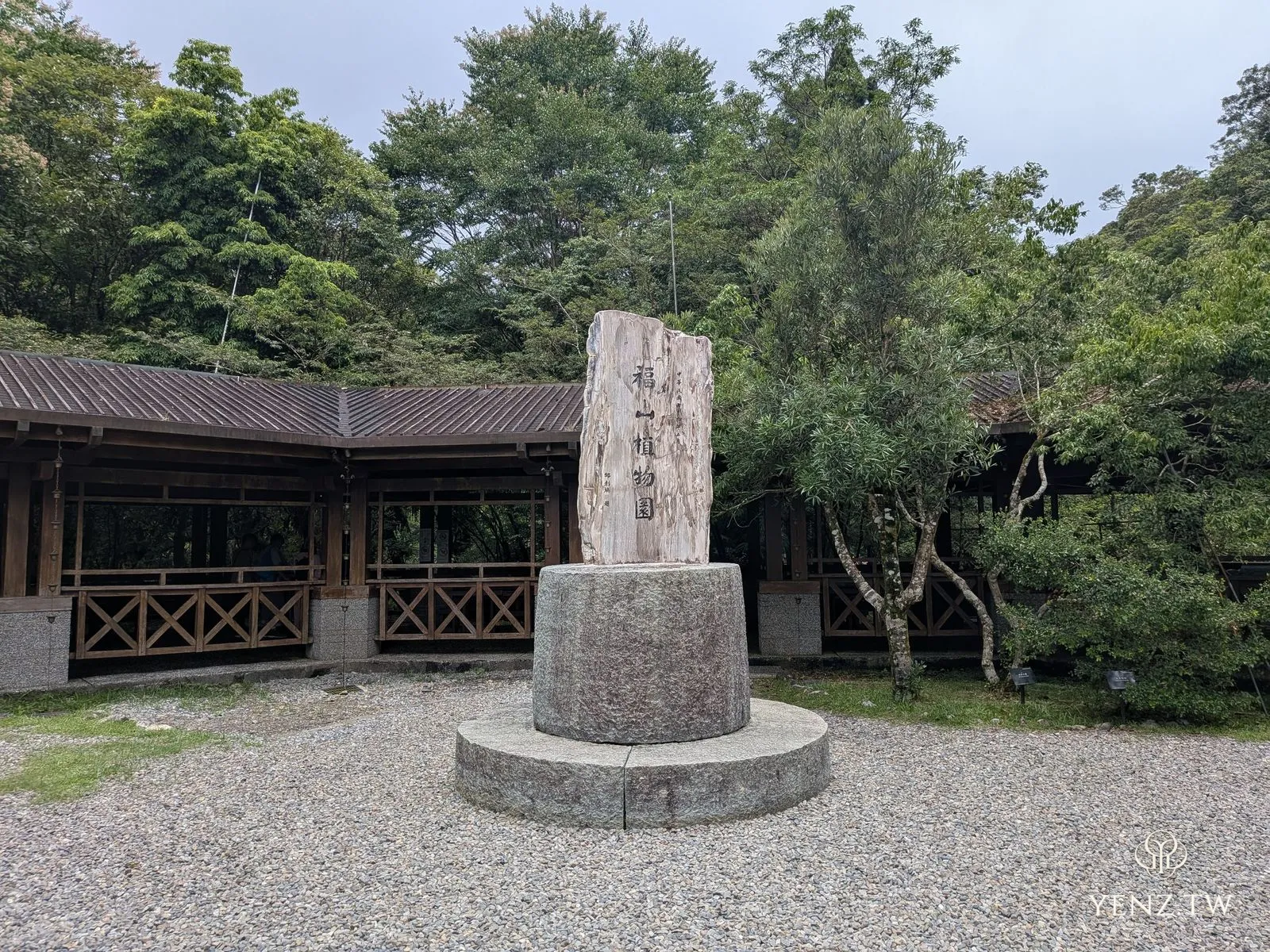 福山植物園的石碑立在圓形石基上，後方是自然中心的木造建築，畫面無人。