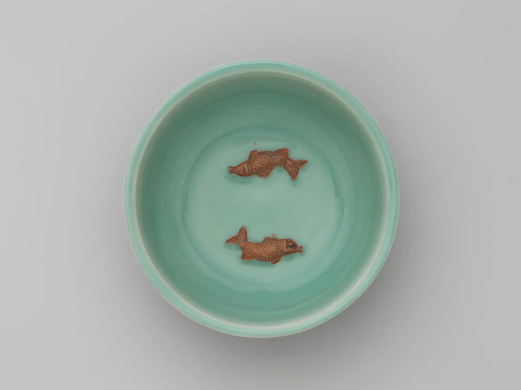 龍泉窯青瓷雙魚碗：粉青色的釉面上，兩尾未上釉的魚以露胎的橘紅色浮在碗心。