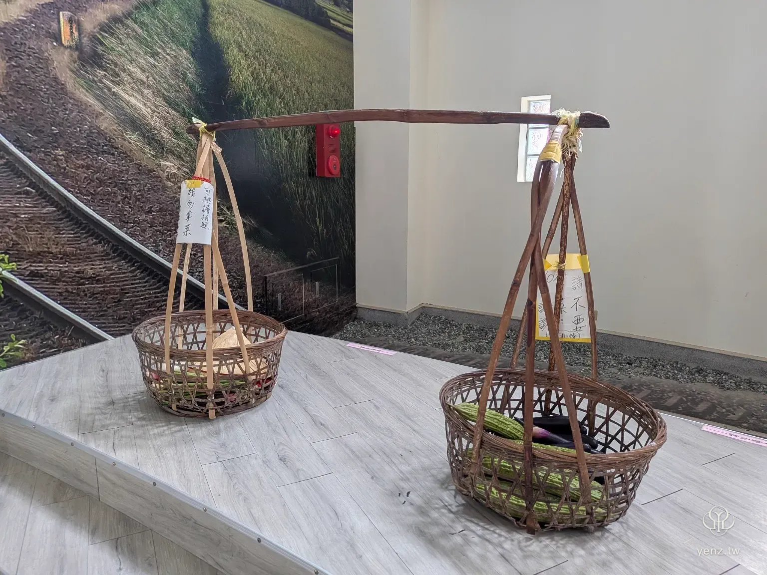挑擔體驗區，竹籃中放有蔬菜模型，背景為農田照片與展示空間。