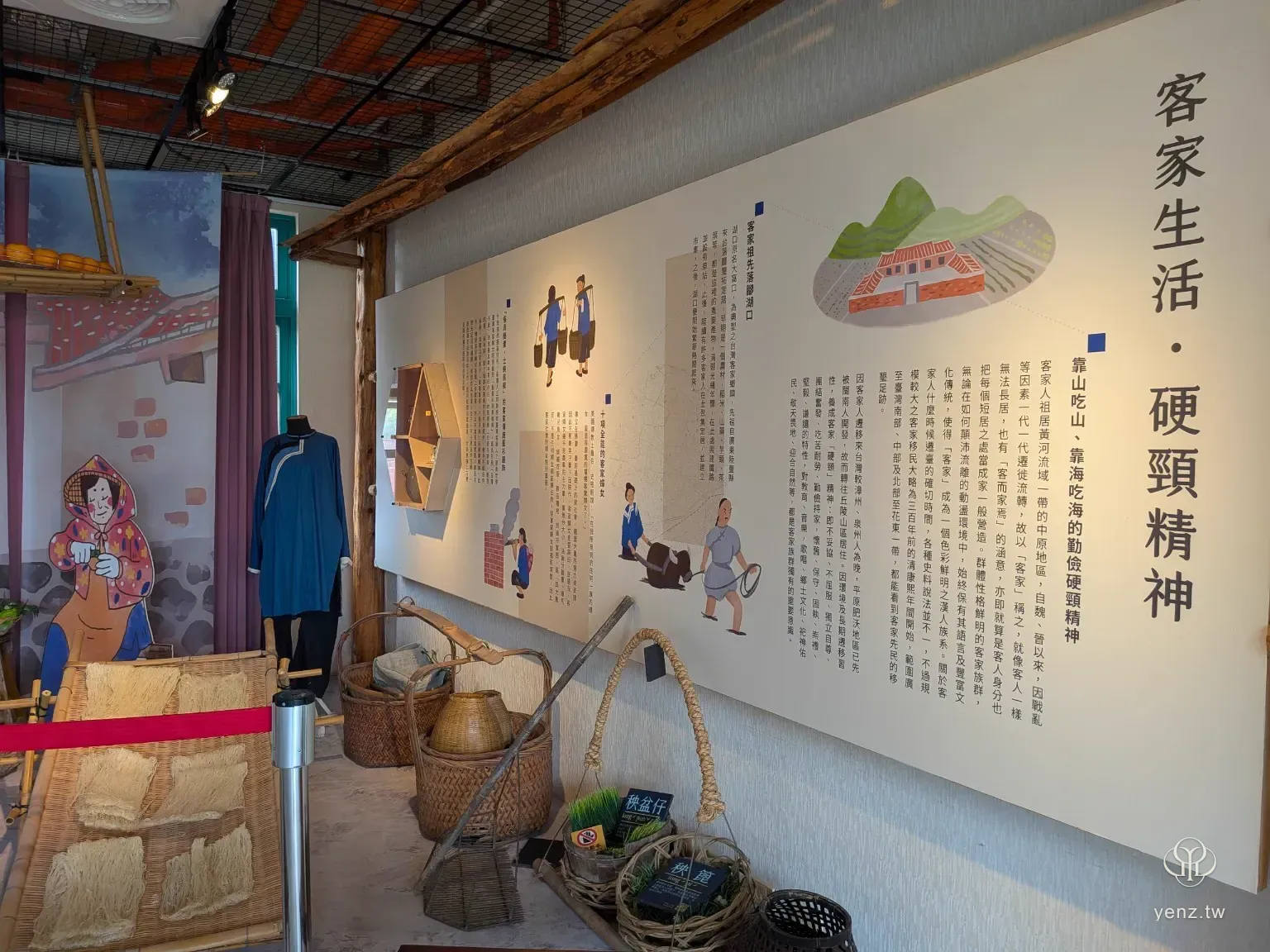客家生活展區，牆面寫有客家生活與硬頸精神，前方展示藍衫、竹籃、農具與挑擔。