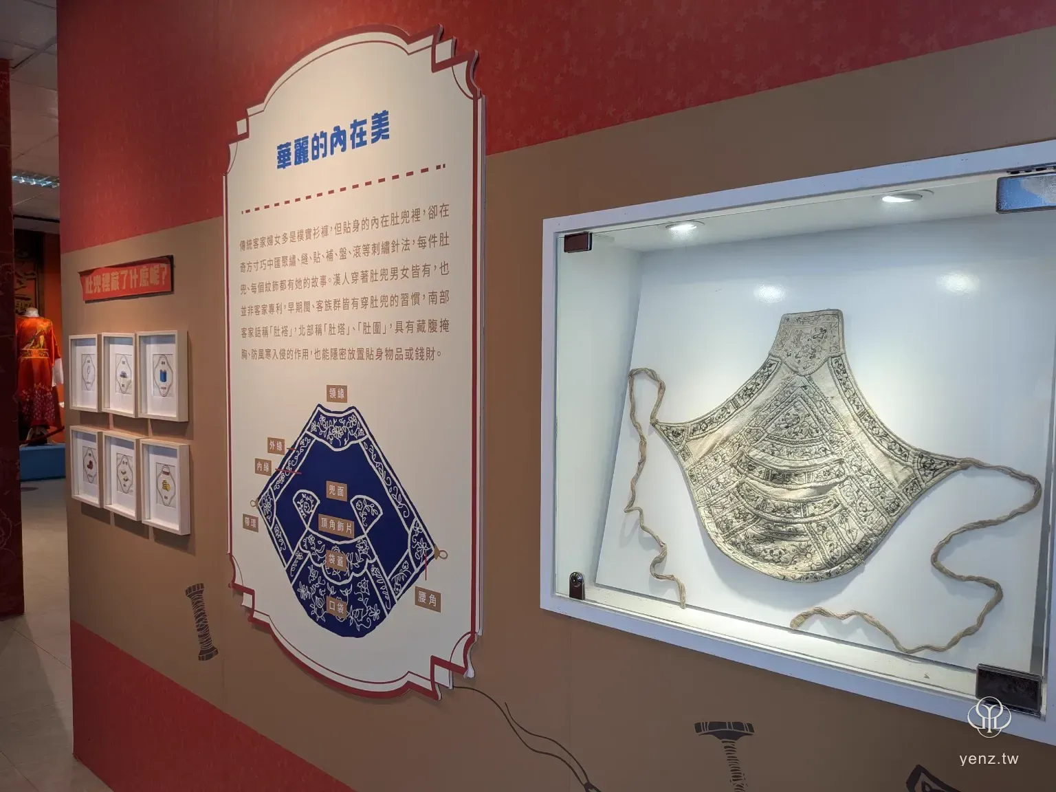 客家肚兜展示牆，右側玻璃櫃中展示一件肚兜，左側有肚兜結構圖與說明文字。