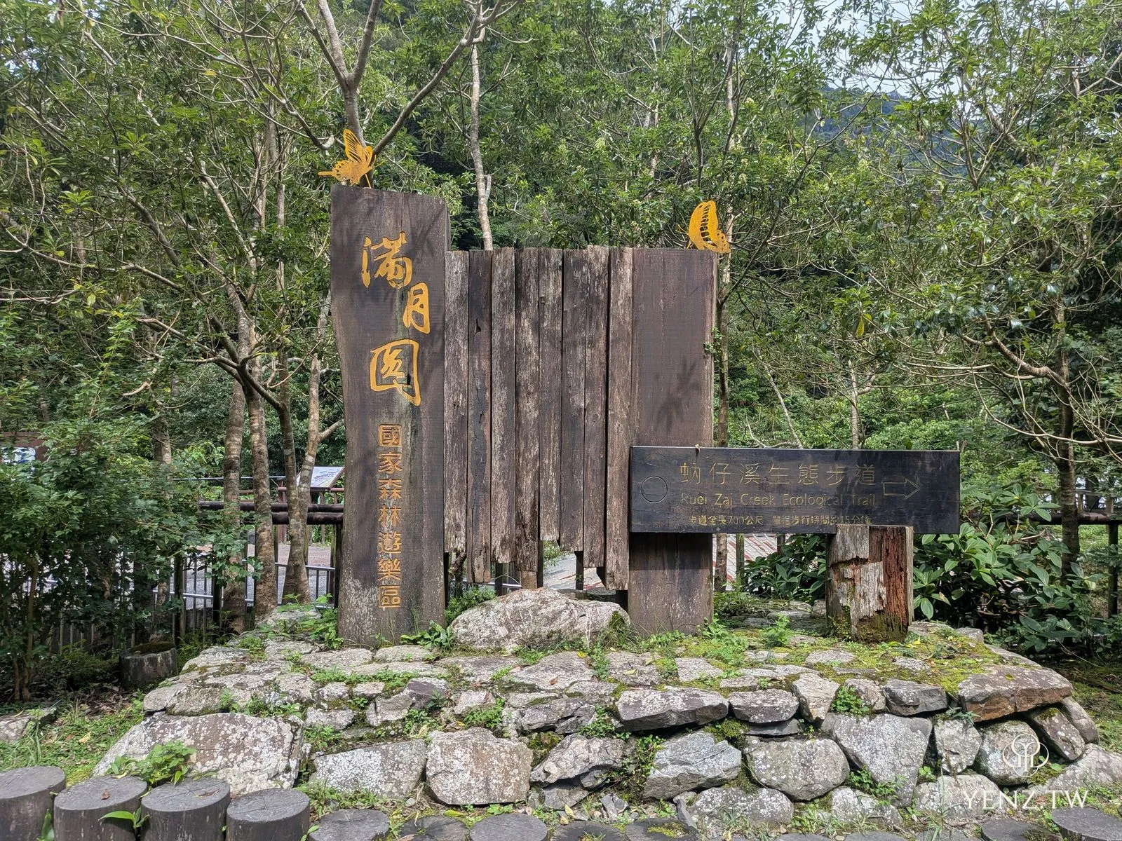 風化原木立板做成的滿月圓入口標誌，金色字體，頂端有金屬蝴蝶。