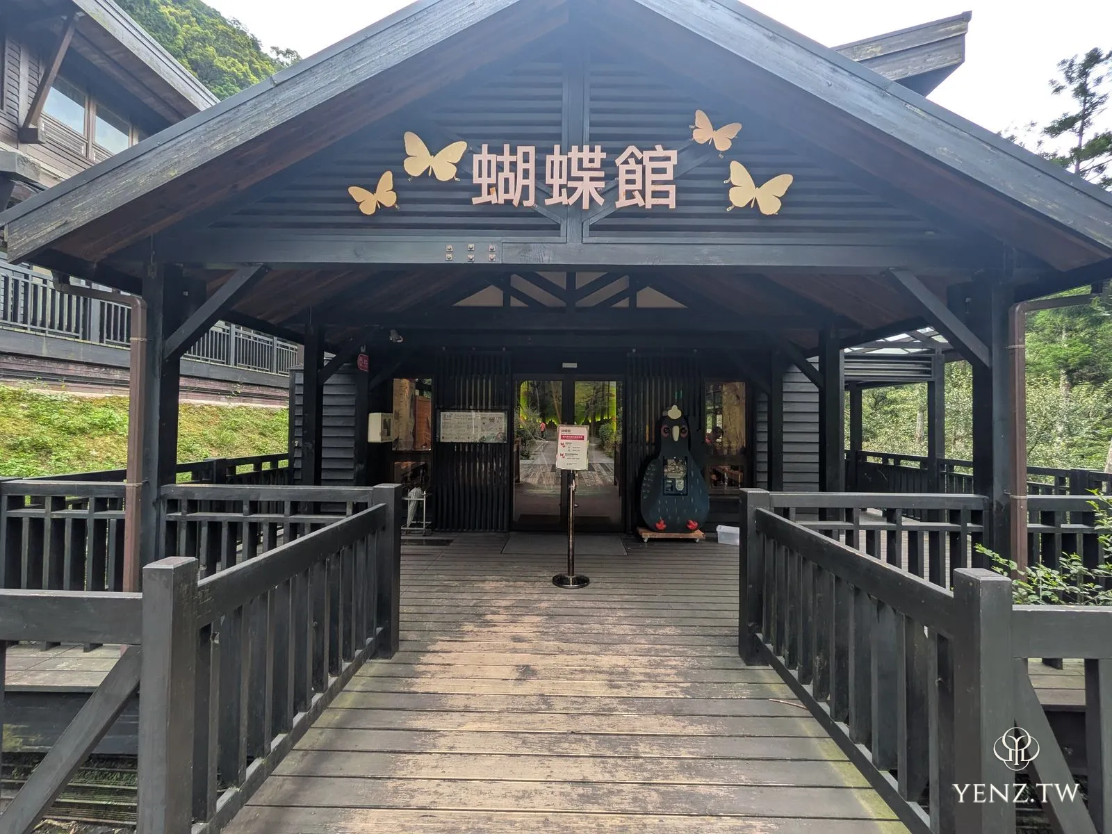 蝴蝶館入口，深色木構建築，門楣上有金色蝴蝶，前方木棧橋。