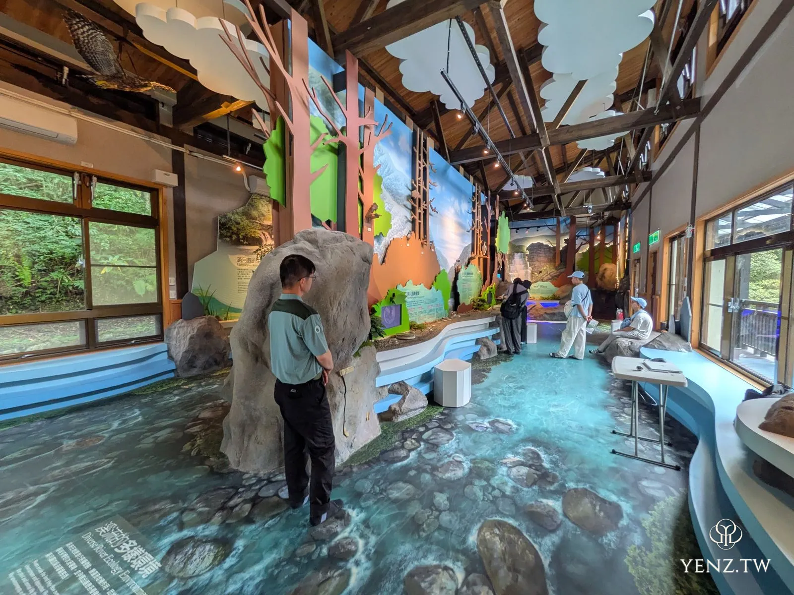 溪流館內部，地板印成溪床，遊客脫鞋走在上面，旁有岩石裝置與溪流壁畫。