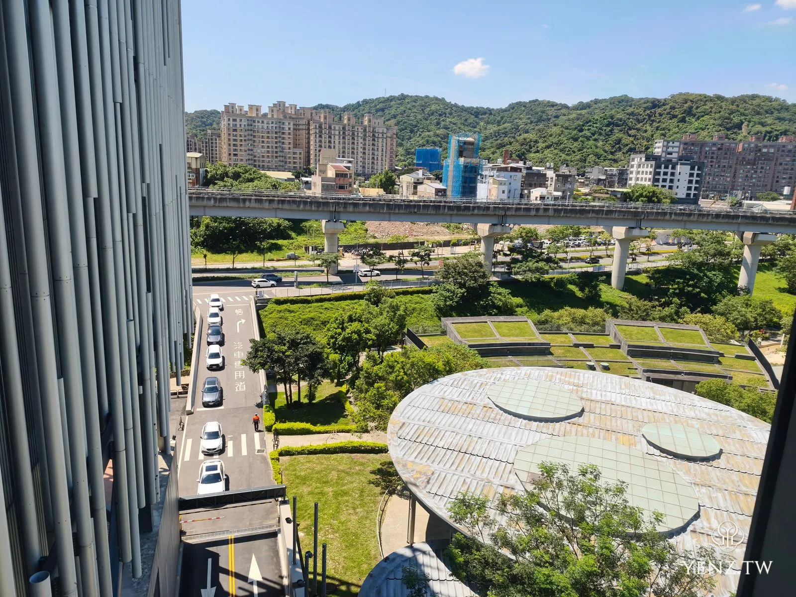 從高處俯瞰，圓形屋頂建築、捷運三鶯線高架橋與大漢溪對岸的社區、遠山。