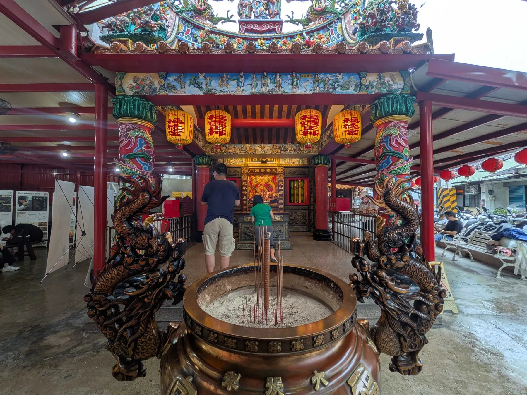 從福德宮香爐前望向廟埕展場，參拜者與展板同框。