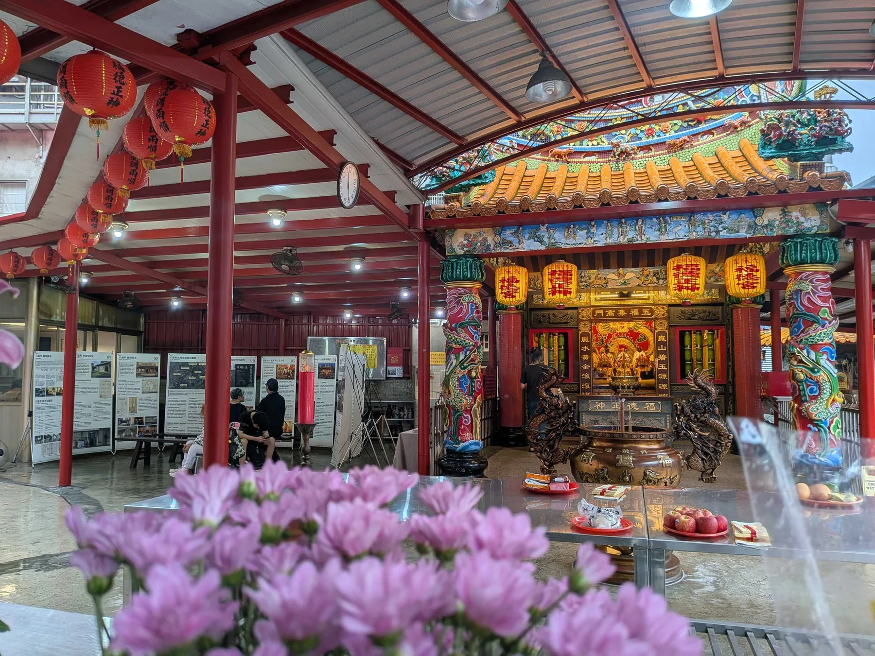 前景是供桌上的粉紅菊花，中景是展板群，右側是福德宮正殿與香爐。