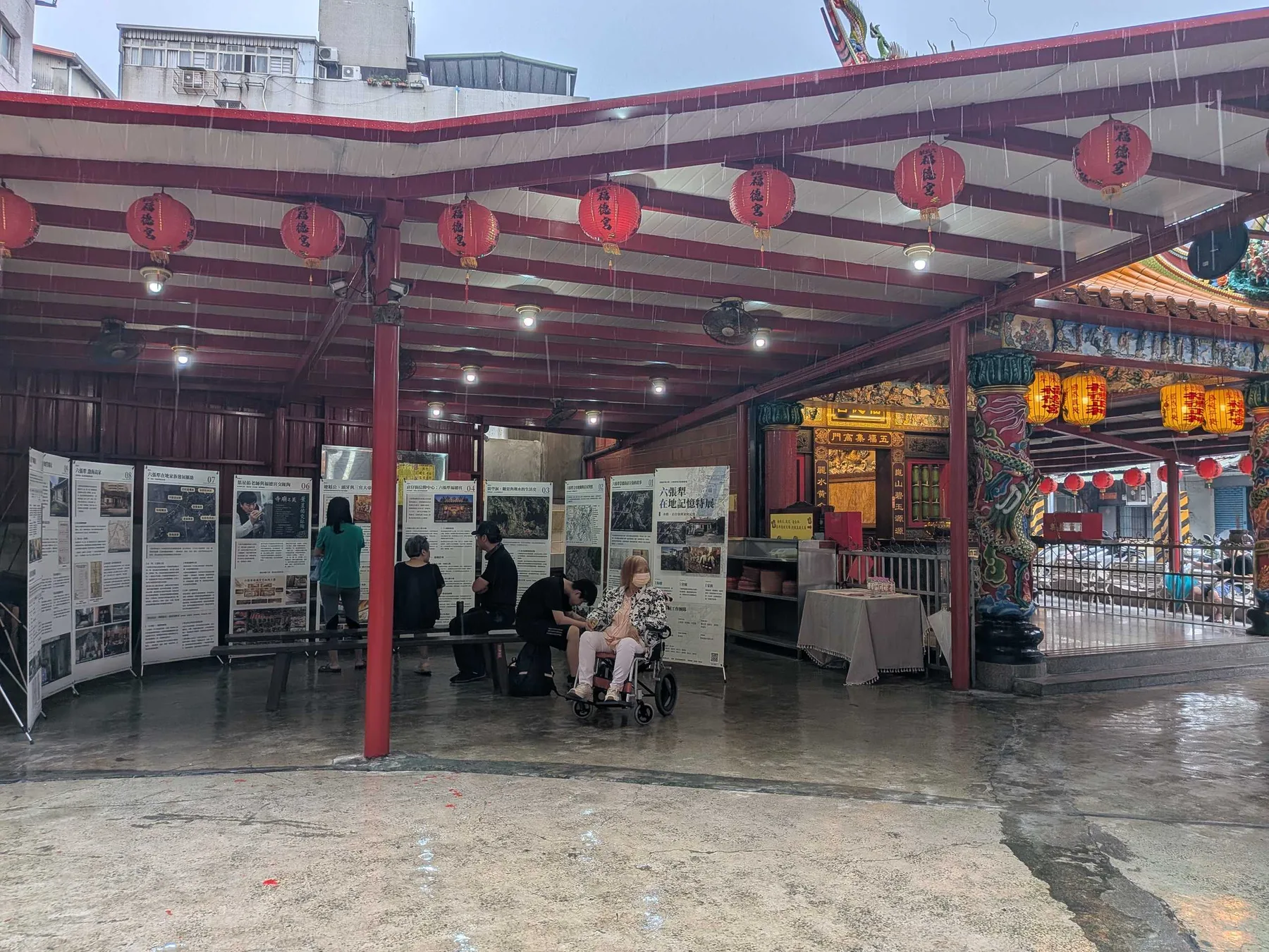 雨中的福德宮廟埕，紅燈籠下觀眾繼續在展板間看展。