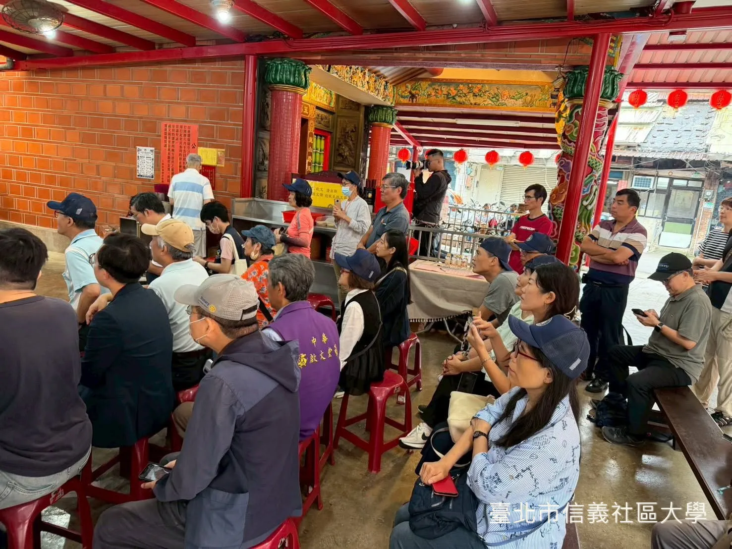 林耿同老師手持麥克風，在家族組展板前為圍坐的觀眾導覽。