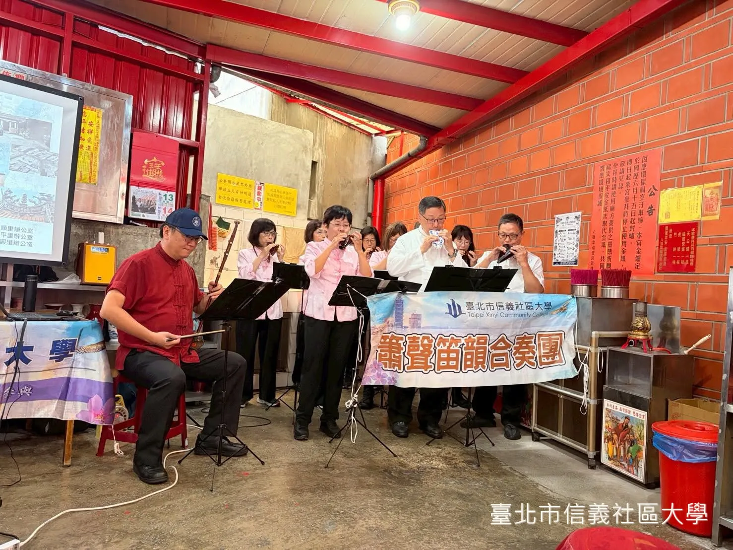 信義社大陶笛社在廟埕演奏，橫幅寫著「臺北市信義社區大學 蕭聲笛韻合奏團」。